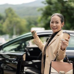 Confident senior business woman disembarking the luxury car with smiling look on camera.