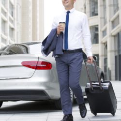 Confident Chinese businessman walking with wheeled luggage